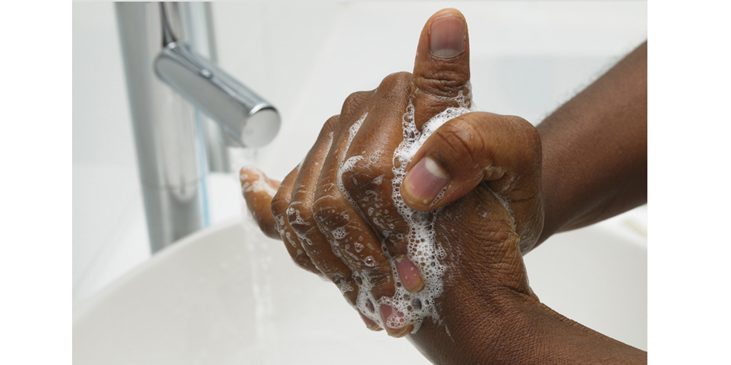 Closeup view of a pair of soapy hands being washed in the foreground over a sink with running water in the background