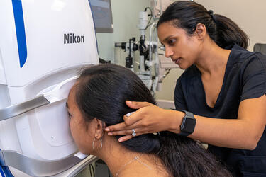 optometrist guides a patiet’s head toward a large retinal scanning device