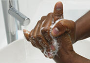 A pair of soapy hands being washed in the foreground over a sink with running water in the background