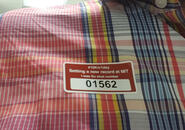 Closeup photo of a sticker with the number 01562 printed on it stuck to a plaid shirt